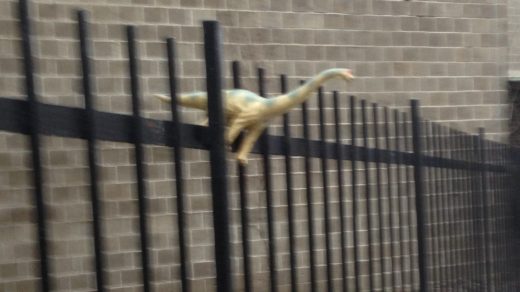 image shows toy dinosaur standing on a fence