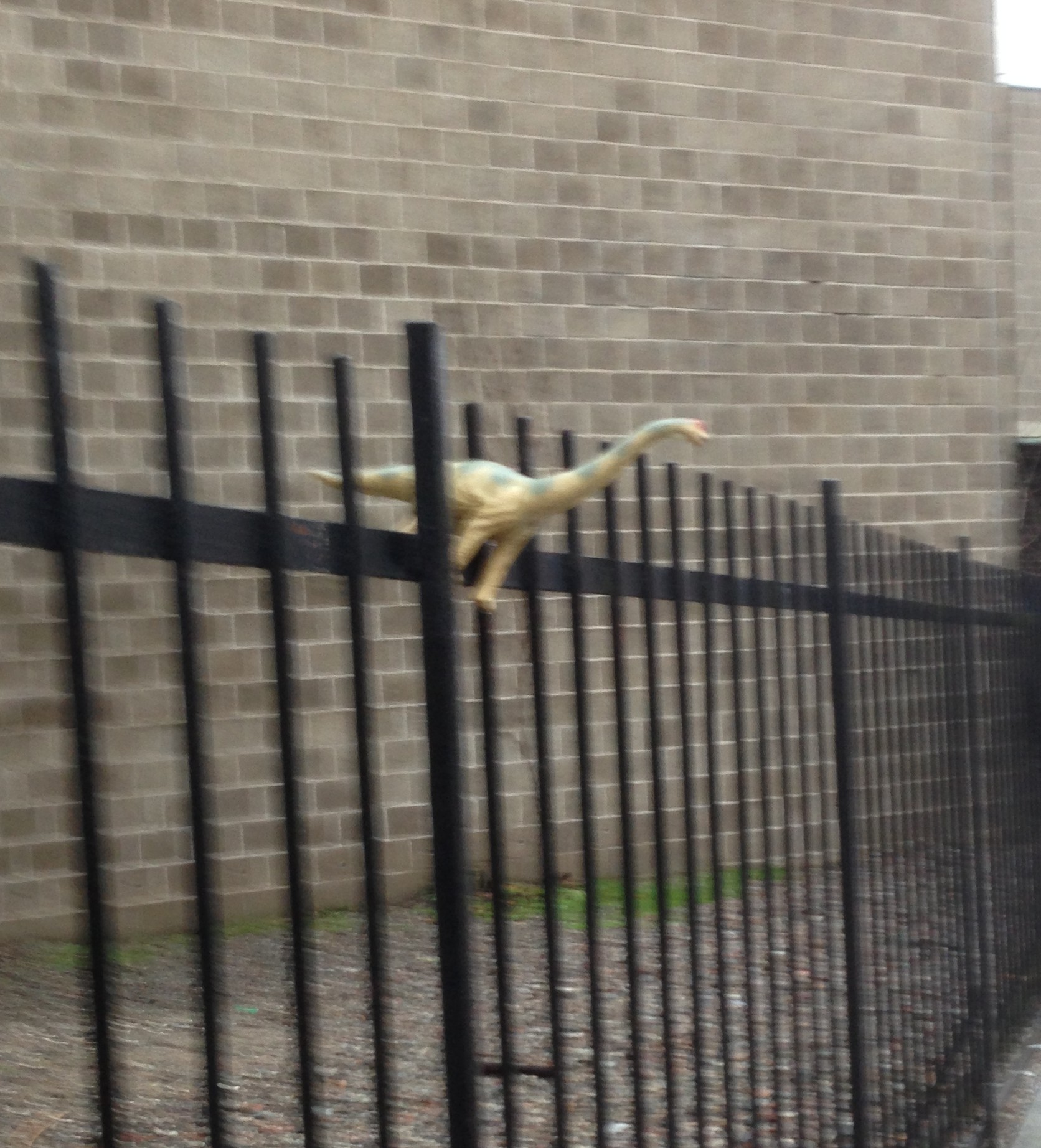 image shows toy dinosaur standing on a fence