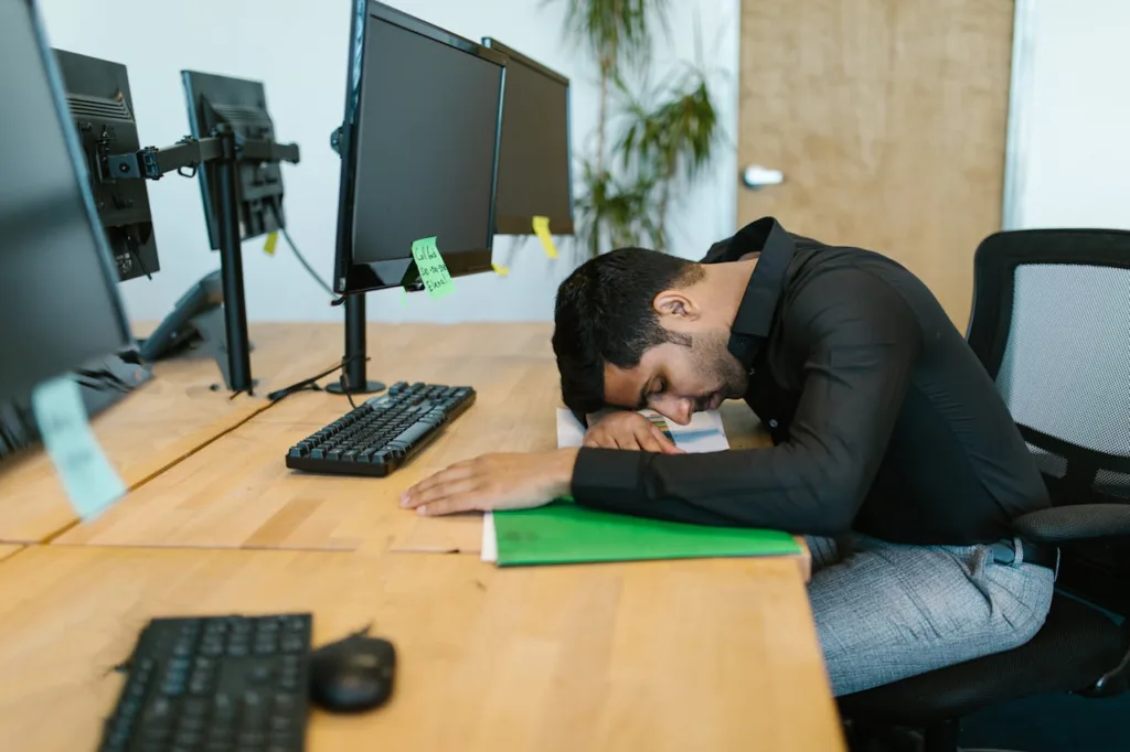 image shows man sleeping at his desk during the in-between days at work